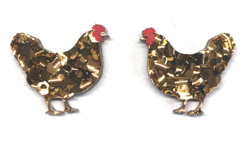 Two rooster-shaped earrings, the Hen Glitter Stud Earrings Bronze by Blue Dog Posters, are made of a gold-colored, glittery material with red combs. The roosters face each other against a white background.