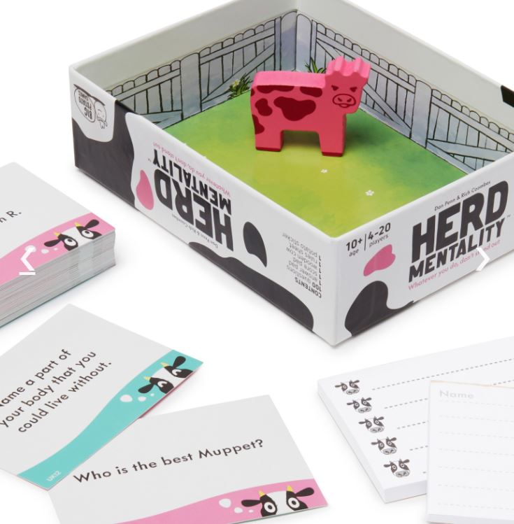 A boxed game titled "Herd Mentality Mini" by Blue Dog Posters is shown. The party game box contains a small pink cow figure and several cards with questions such as "Who is the best Muppet?" and "Name a part of your body that you could live without." There's also a notepad with sheets labeled "Name." Perfect for any family game night!