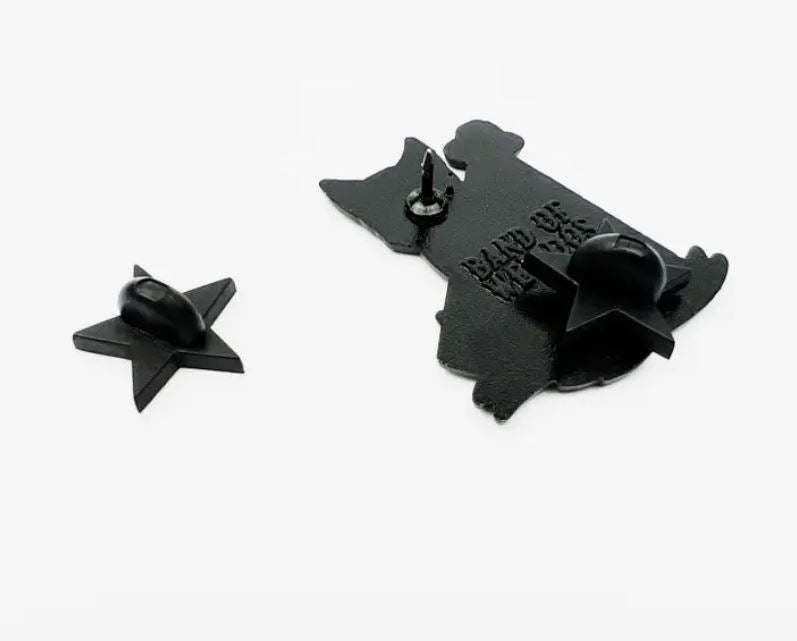 The "I Want to Believe Fox Enamel Pin" from Blue Dog Posters, featuring a black metal pin in the shape of a dog with two pin posts and a black star-shaped backer, is displayed against a plain white background.
