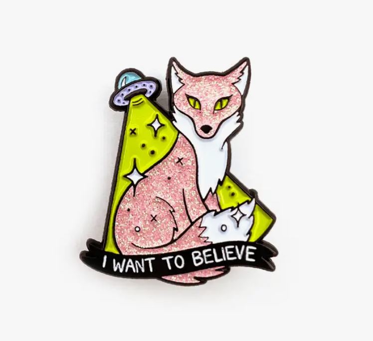 Introducing the "I Want to Believe Fox Enamel Pin" by Blue Dog Posters, featuring a pink fox seated alongside a smaller white fox under a UFO's beam. The background showcases stars and cosmic elements, with the text "I WANT TO BELIEVE" displayed at the bottom. Crafted in hard enamel for vibrant color and durability.