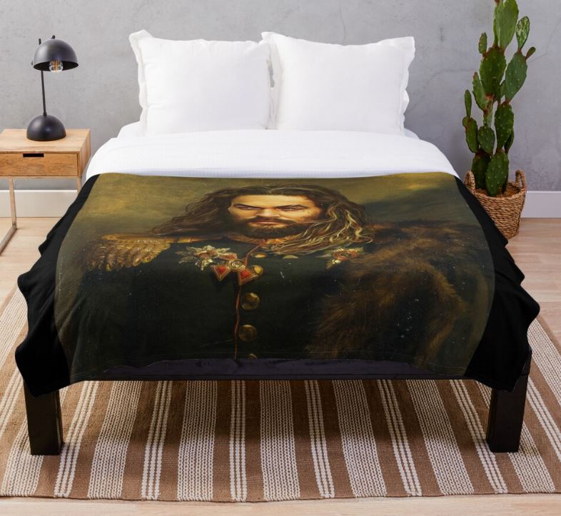 A modern bedroom flaunts a bed with a black frame, adorned with the Jason Momoa Replace Face Throw Blanket by Blue Dog Posters, showcasing a painting of Jason Momoa in a military-style coat. The room includes white pillows, a wooden nightstand holding a black lamp, a green cactus, and is completed by a striped rug.