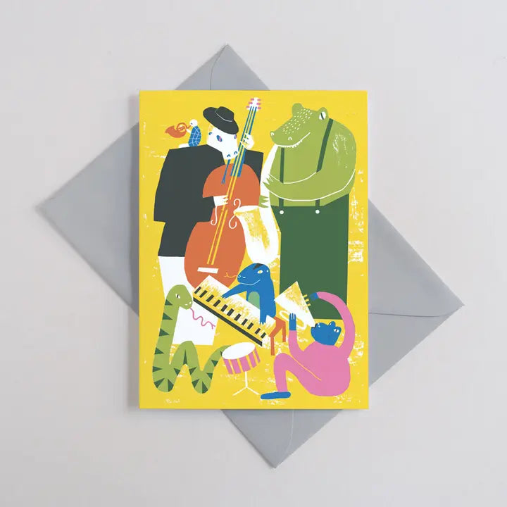 The Jazzy Reptiles Greeting Card by Blue Dog Posters features a vibrant scene of animal friends playing instruments, printed on plastic-free yellow card and comes with a gray envelope.