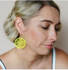 A woman with short blonde hair wears Denz Citrus Slice Earrings in Lemon by Blue Dog Posters. She gazes downward with a calm expression, set against a soft, neutral background.