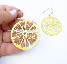 Close-up of hands holding Blue Dog Posters' Denz Citrus Slice Earrings in Lemon, featuring a thin yellow design with intricate cut-out patterns resembling citrus segments.
