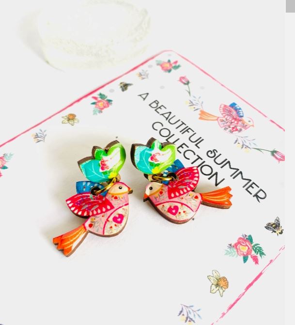 Love Bird Retro Earrings by Blue Dog Posters, featuring intricate bird designs, rest on a card titled "A Beautiful Summer Collection," decorated with floral illustrations.