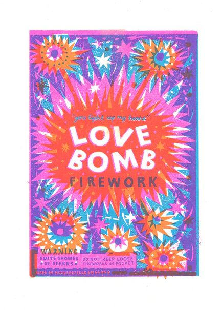 The Love Bomb A4 Print by Printed Peanut from Blue Dog Posters features colorful firework packaging with vibrant explosions in pink, orange, blue, and purple hues. The text on the print reads: "You light up my heart," along with "LOVE BOMB FIREWORK." A warning label states: "Emits shower of sparks. Do not keep loose fireworks in pocket.