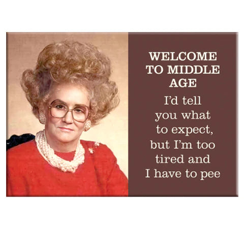 A woman with big hair, glasses, and a red outfit poses by a sign that says, "WELCOME TO MIDDLE AGE..." on the Blue Dog Posters "Welcome to Middle Age Magnet.