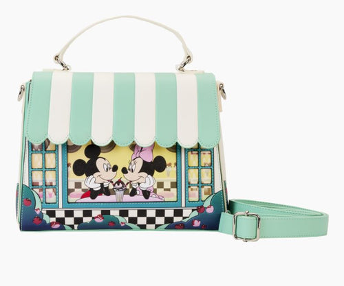 The Disney Mickey & Minnie Date Diner Crossbody by Blue Dog Posters showcases a stylish handbag with Mickey Mouse and Minnie Mouse sharing a cupcake in a cafe scene. This bag is predominantly pastel green and white, featuring striped details and floral designs. It includes both a top handle and an adjustable shoulder strap for versatile carrying options.