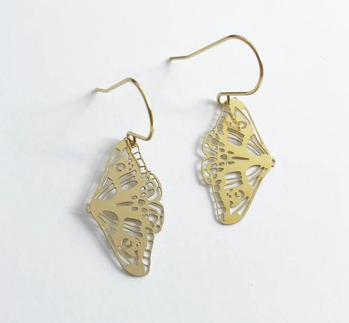 The Denz Mini Earrings Moth Gold, crafted by Blue Dog Posters from recycled plated stainless steel, are showcased against a white background. These gold moth-shaped earrings feature intricate cut-out designs and hang from surgical steel hooks, highlighting the delicate, detailed craftsmanship in the wings.