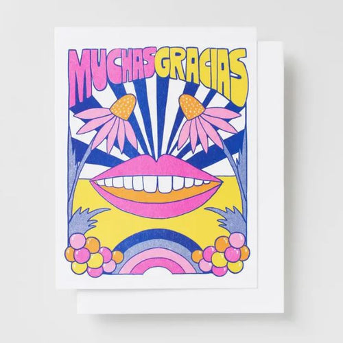 The "Muchas Gracias Risograph Card" by Blue Dog Posters is a vibrant greeting card printed with veggie-based inks. It showcases the Spanish words "Muchas Gracias" at the top in bold pink and yellow letters. The whimsical design features a large smiling mouth, flower eyes, and colorful abstract shapes in yellow, blue, and pink hues on recycled paper.