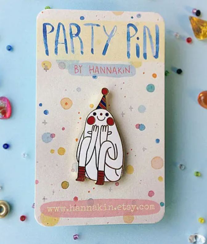 A whimsical hard enamel Party Pin Enamel Pin by Blue Dog Posters, illustrating a character in a party hat with hands on cheeks, is attached to a pastel-colored card that reads "Party Pin by Blue Dog Posters." The card, adorned with colorful dots and the URL "www.hannakin.etsy.com," showcases this Melbourne-made treasure.
