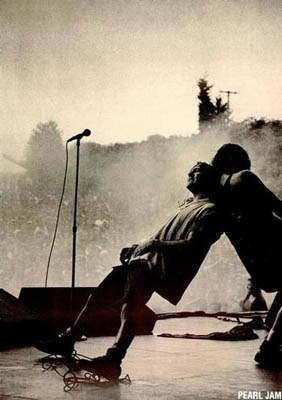 Two musicians perform energetically on an outdoor stage, one leaning into the other, amid haze and vibrant colors. "Pearl Jam Live" by MUS 291 is written in the bottom corner for a classic Rock Poster look.