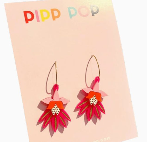 A pair of vibrant pink and orange flower-shaped earrings with gold hoops displayed on a pastel pink card labeled "Blue Dog Posters" and named "Dancing Blooms Pink & Orange Earrings.