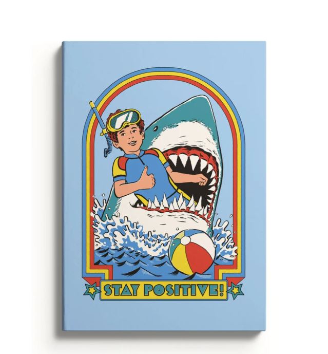 An illustration of a smiling child in snorkel gear, playfully interacting with a shark and a colorful beach ball, is featured on the A5 Soft Cover Notebook - Stay Positive by Blue Dog Posters, with bold text reading "Stay Positive!.