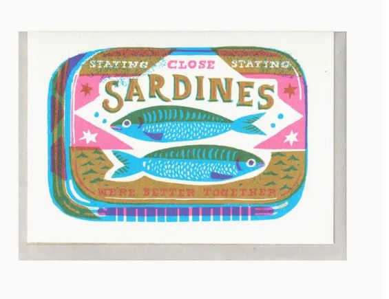 Illustration of a sardine can label with a retro design. The label reads, "Sardines Riso Card by Blue Dog Posters. We're better together." The label features two sardines in the center with stars and geometric patterns in pink, blue, and green. Packaged with a sustainably sourced card inside a biodegradable cello bag.