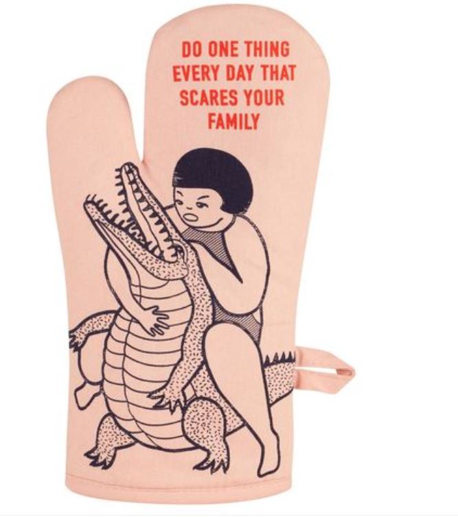 The "Scares Your Family" oven mitt by Blue Dog Posters is a super-insulated pink mitt featuring a black-and-white illustration of a person wrestling an alligator. Bold red text above the image reads, "DO ONE THING EVERY DAY THAT SCARES YOUR FAMILY," and it includes a convenient loop for hanging on the side.