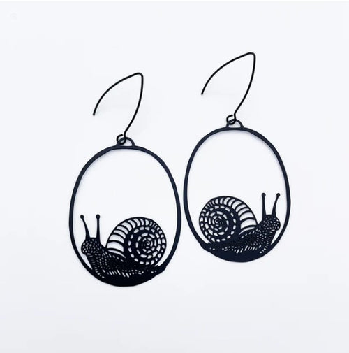 Blue Dog Posters' Snails in Black Dangle Earrings feature intricate, whimsical snail designs nestled within oval-shaped frames. The detailed spiral shells and elongated bodies of the snails are highlighted against a white background, making them perfect for gardener's jewelry enthusiasts. These statement earrings are suspended by thin hooks.