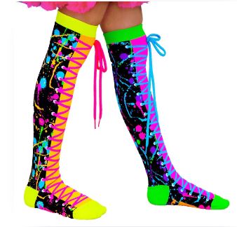 A person's legs are adorned with Madmia Colour Run Socks by Blue Dog Posters, featuring bright, multicolored splash designs and faux lace-up patterns. The left sock flaunts neon pink laces, while the right sock boasts blue neon shoelaces. Both socks showcase neon yellow and green toes and heels set against a black background.