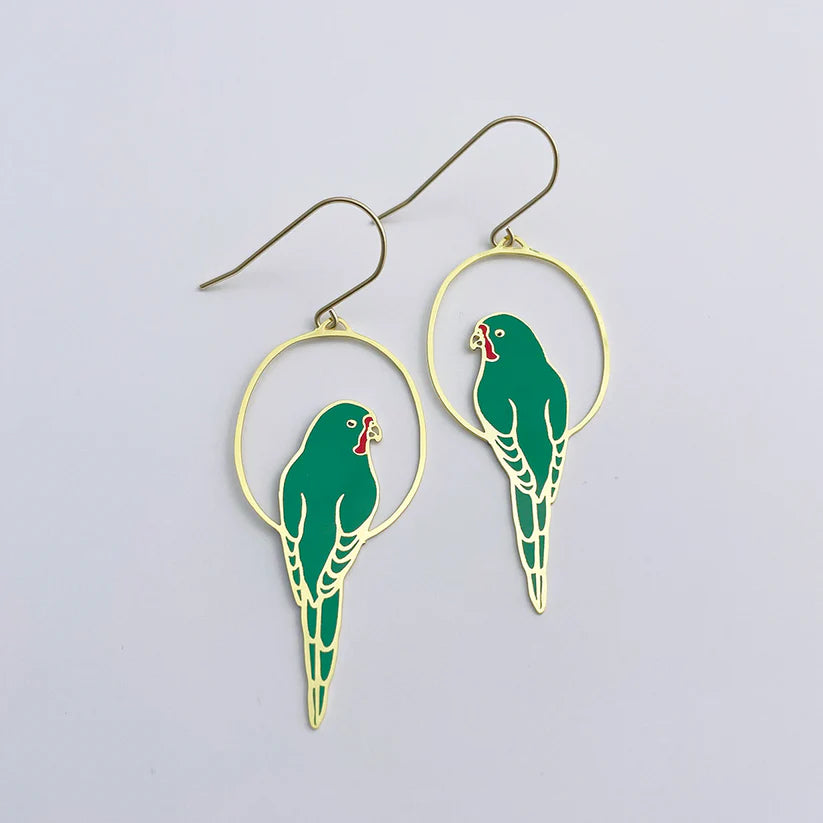 Introducing the Parrot in Green Denz Earrings by Blue Dog Posters: This pair of lightweight earrings features intricate green parakeet designs perched on circular gold-toned frames. With their vibrant red beaks and fine detailing, these earrings create an elegant Australiana accessory and are presented on a plain white background.
