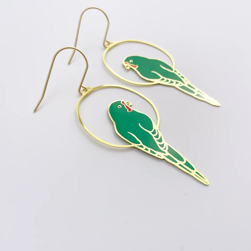 The Parrot in Green Denz Earrings from Blue Dog Posters feature gold hooks with circular gold frames encasing green parrot pendants. The parrots are intricately detailed with yellow accents and red beaks, making them perfect Australiana accessories. These lightweight earrings are set against a plain light grey background.