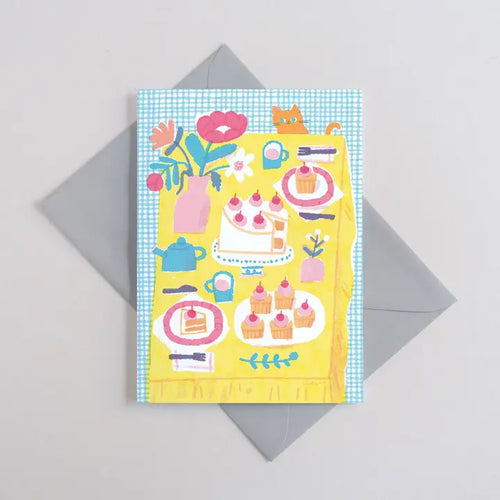 The Tea Party Greeting Card by Blue Dog Posters (Printer Johnson) is a colorful A6 card with illustrated cakes, cupcakes, a teapot, cups, flowers, and a cat on a yellow tablecloth over a blue checked background. Includes gray envelope.