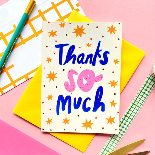 The Thanks So Much Greeting Card by Blue Dog Posters features “Thanks so much” in blue and pink letters with orange stars and dots, displayed on a yellow envelope against a pink background with stationery items.