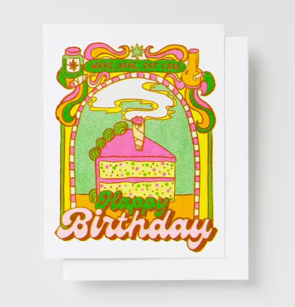 The HBD Wake Bake Cake Risograph Card by Blue Dog Posters showcases a vibrant birthday scene with a slice of pink and green cake, complete with a lit candle and smoke curling above. The card is printed using eco-friendly veggie-based inks. The playful fonts exclaim "Make, Bake, Eat Cake" at the top and "Happy Birthday" at the bottom, surrounded by a whimsical decorative border.