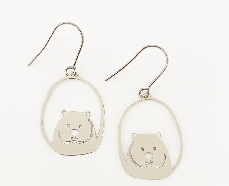 The Denz Mini Earrings Wombat Silver by Blue Dog Posters are silver hook earrings crafted from recycled plated stainless steel. They feature a circular design with cutout illustrations of wombats in the center, depicted in a minimalist style showing only their heads and ears against a plain white background.