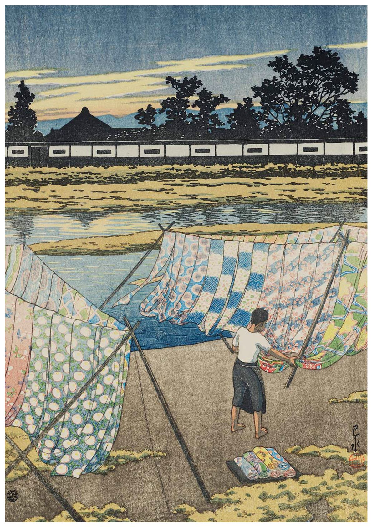 A person hangs a variety of colorful fabrics on a line to dry by a riverbank under a partly cloudy sky. Trees and a white building with a dark tiled roof are visible in the background, reminiscent of an exquisite A3 490 Evening at the Kamo River printed on high-quality 250gsm Satin Paper.