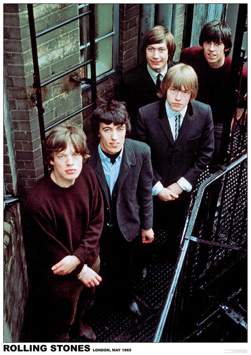 A vintage photo of the Rolling Stones taken in London, May 1965. The five band members are standing on a metal staircase by a brick wall, looking up at the camera. They are dressed in casual and formal attire, blending mid-60s fashion styles—a perfect addition to any music collection or rock poster display with The Rolling Stones 1965 by MUS 281.