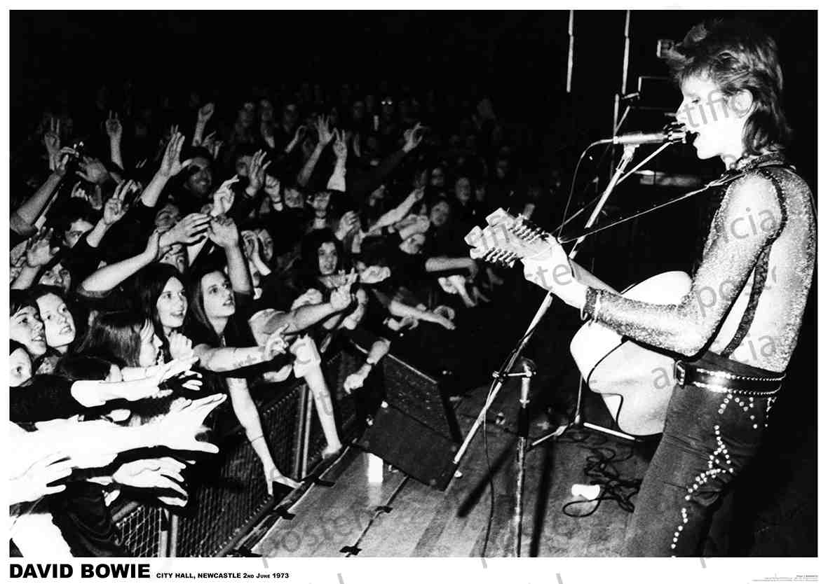 Black and white photo of a concert showing a musician, playing an acoustic guitar and singing into a microphone, with enthusiastic fans reaching out from the audience. Printed on premium 150gsm gloss paper, this David Bowie Newcastle 1972 rock poster's caption reads “DAVID BOWIE CITY HALL, NEWCASTLE 26 June 1973.” A must for any music collection from MUS 095.