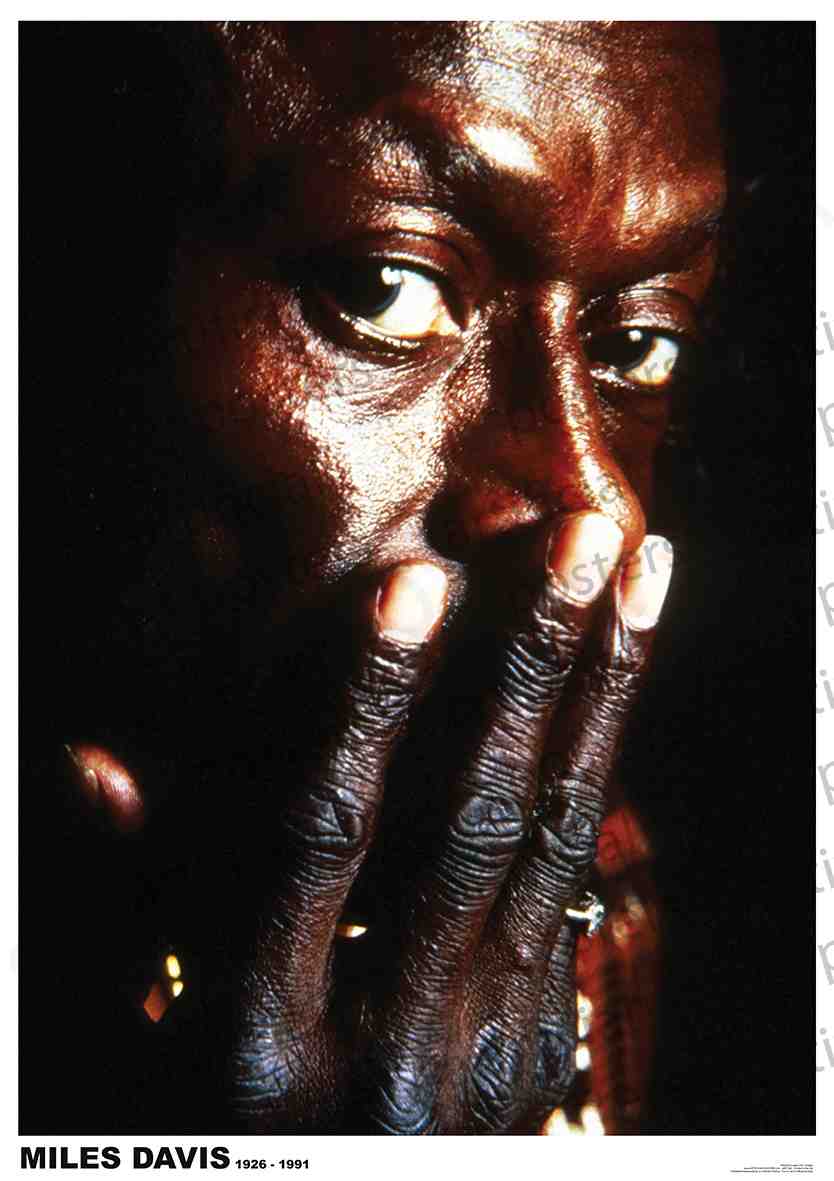 Close-up photo of a man partially covering his face with his hand, gazing intently at the camera. The man has intense eyes and dark, weathered skin. Text at the bottom reads "Miles Davis 1926 - 1991." Perfect addition to any Jazz Poster collection or Large Regular Posters for music enthusiasts. Brought to you by MUS 087.