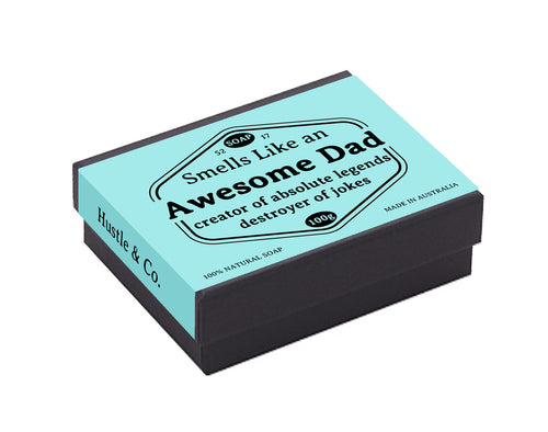 A light blue soap box labeled "Hustle and Co Soap - Awesome Dad" by Blue Dog Posters reads "Smells Like an Awesome Dad - creator of absolute legends! destroyer of jokes." The 100g Australian-made soap, crafted with natural Goat’s milk in Australia, comes in a black box with a teal top that says "Hustle & Co Soap.