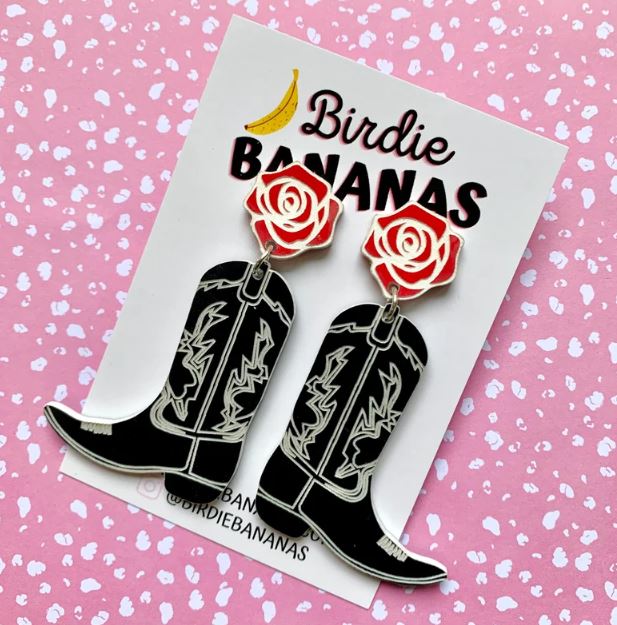 Displayed on a card adorned with a small banana graphic and "Birdie Bananas" at the top, this pair of Cowboy Boots Acrylic Earrings in Black from Blue Dog Posters features intricate white designs and red rose studs. These fun, quirky accessories are showcased against a pink surface with white speckles, highlighting our handmade jewellery collection.