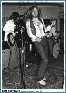 A black and white photo of the band Led Zeppelin performing on stage in 1969. The lead singer is energetically dancing and singing into a microphone, perfect for any Music Collection. A guitarist and bassist are playing their instruments in the background amidst various musical equipment, creating an iconic MUS 313 Led Zeppelin.