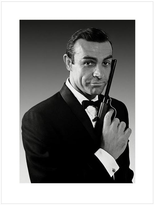 Black and white portrait of a man in a tuxedo, holding a handgun vertically with the barrel pointing upward, close to his face. With a confident expression against a gradient background, this piece is part of our Pop Culture Themed Art in the Contemporary Art Collection. Introducing James Bond - Sean Connery by MEZ 240.
