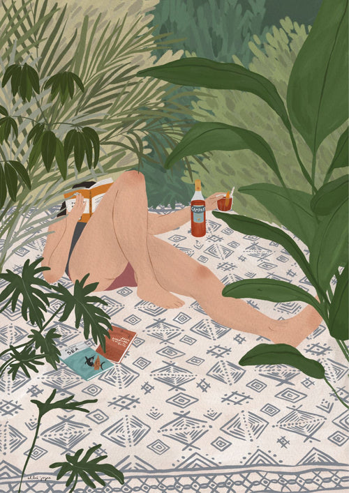 A person is lying on a patterned mat surrounded by lush green foliage. Their face is obscured by a book they're reading, and there are various snack items and beverages, including a bottle of Spritz Me by Chloe Joyce. This scene, part of the fap Featured Artists Collection, depicts a relaxed outdoor setting.