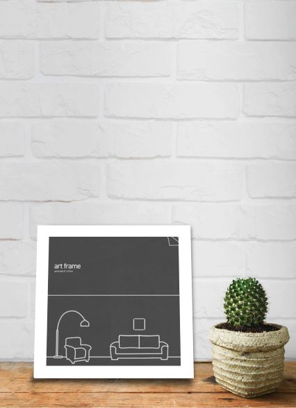 A Classic Frame Square 21 x 21cm White from Blue Dog Posters with minimalist furniture outlines stands on a wooden surface against a white brick wall. Beside the frame is a small potted cactus in a textured beige planter. The scene combines sleek decor with a touch of nature.