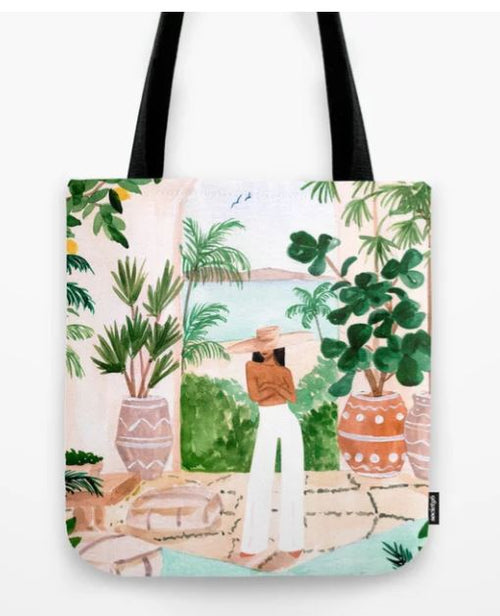 The Blue Dog Posters Tote Bag 40x40cm Peaceful Morocco features a sublimation printed illustration of a person standing on a terrace adorned with potted plants. The person, wearing a hat, an orange top, and white pants, gazes out at a scenic view of the ocean and distant mountains, surrounded by lush foliage.