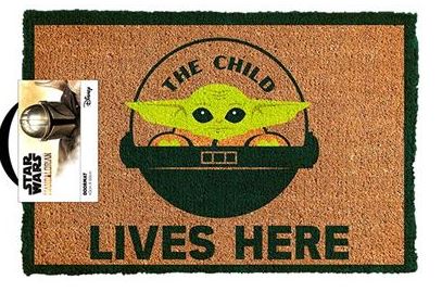 A rectangular coir doormat with a green border featuring an image of "The Child" from Star Wars in the center, accompanied by the text "THE CHILD LIVES HERE" below. Part of the Homewares Collection, a corner tag displays official Blue Dog Posters Mandalorian The Child Lives Here Doormat branding.