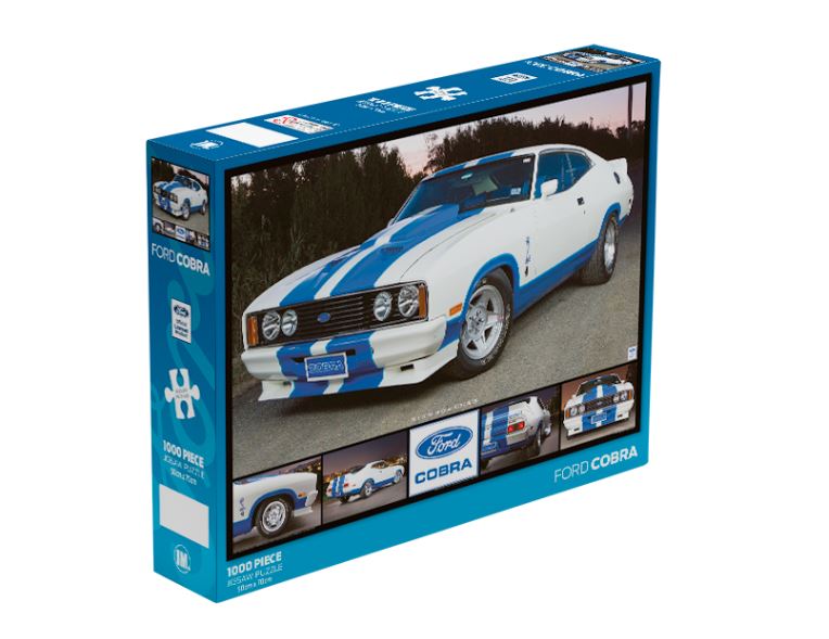 A 1000-piece jigsaw puzzle box features an image of a classic Ford Cobra car with blue racing stripes. The blue-bordered, officially licensed giftware displays the puzzle image on the front along with multiple smaller images of the car and branding elements on the sides. This is the Ford Cobra 1000pc Puzzle from Blue Dog Posters.