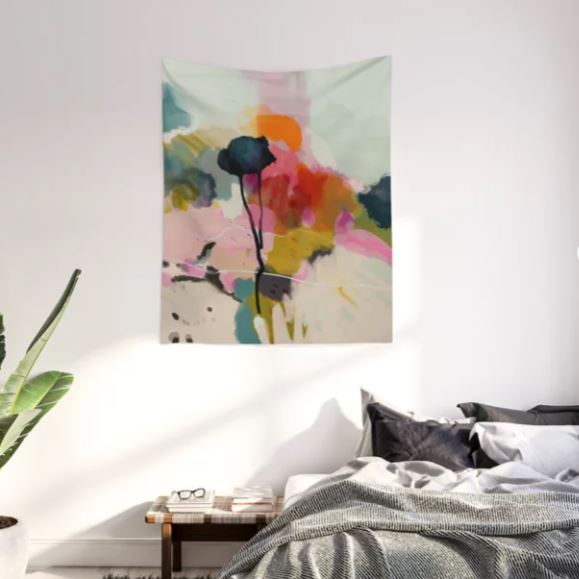 A modern bedroom with the Paysage Abstract Art Textile Lge by Blue Dog Posters on the wall above a bed. The bed is adorned with a gray and white comforter and black pillows. A small bedside table, featuring a book and a potted plant, sits next to the bed. A larger plant is positioned in the left corner of the room.