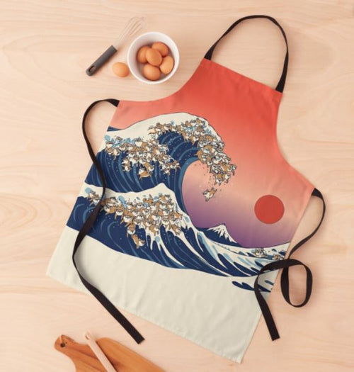 The Great Wave of Shiba Inu Apron by Blue Dog Posters showcases a stylized, colorful design inspired by "The Great Wave off Kanagawa," featuring Shiba Inus riding the wave against a pinkish-orange sky and a red sun. This machine washable apron from our Homewares Collection is laid flat on a light wooden surface, surrounded by kitchen utensils and eggs.