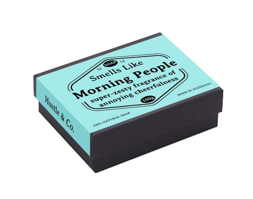 A light blue and black rectangular soap box labeled "Hustle and Co Soap - Morning People," with a tagline "Super-zesty fragrance of annoying cheerfulness." This 100g Goat's milk soap, perfect for natural skincare and eczema relief, is displayed with the brand name "Blue Dog Posters" and marked "Made in Australia.