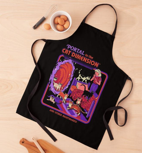 Displayed on a wooden surface with a bowl of brown eggs and a fork nearby, the Steven Rhodes Cat Portal Apron by Blue Dog Posters features a vibrant design with cats emerging from a portal, a woman playing guitar, and the text "Portal to the Cat Dimension and Other Nightmares!" This black apron from our homewares collection is machine washable.