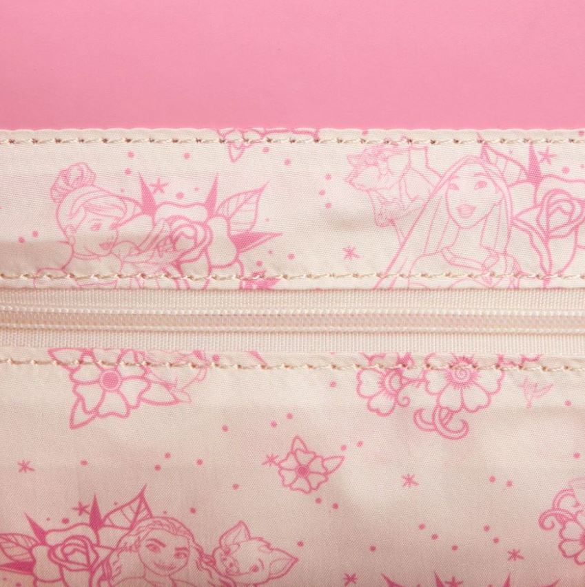 A close-up view of a light pink patterned fabric, featuring outlines of various princesses and floral designs in a darker pink. The top portion of the fabric includes a zipper with neat stitching. This Blue Dog Posters Disney Princess Floral Tattoo Crossbody is crafted from vegan leather, set against a bright pink background.