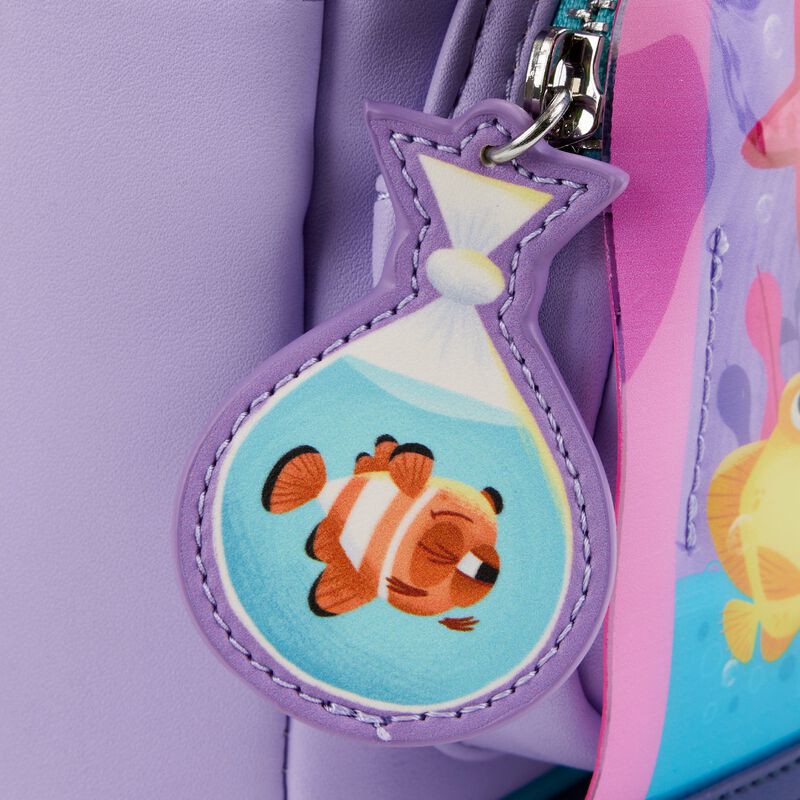 A close-up of the Finding Nemo Darla Mini Backpack by Blue Dog Posters, adorned with a charming accessory in the form of a plastic bag holding a cartoon clownfish. This delightful charm brings to mind the iconic Darla Fish Tank scene from Finding Nemo. The backpack's design includes vibrant colors, and the clownfish sports classic white and orange stripes.