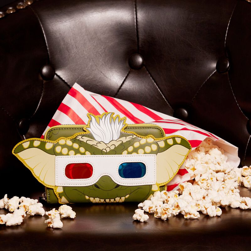 A whimsical, stylish "Gremlins Stripe Pop Purse" by Blue Dog Posters featuring a character with 3D glasses, positioned on a dark leather chair. Surrounded by a red and white striped bag spilling popcorn, the purse incorporates glow-in-the-dark details for a playful, movie-themed scene reminiscent of the Funko Pop! designs by Loungefly.