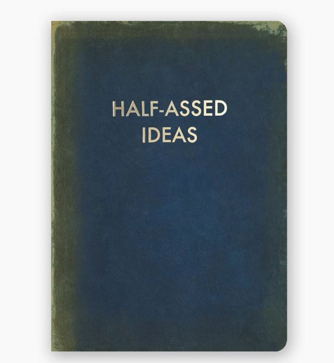 A dark blue, slightly worn notebook by Blue Dog Posters with the title "Half Assed Ideas Journal" printed in uppercase gold foil letters centered on the cover. This useful journal features dotted pages, perfect for organizing your thoughts.