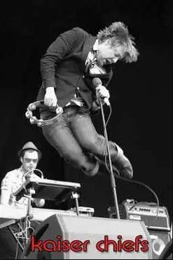 Black and white image of a band performing on stage. The lead singer, mid-jump, holds a tambourine and a microphone. Another band member is playing a keyboard in the background. The text "Kaiser Chiefs" appears at the bottom in red font, making this MUS 207 rock poster a standout addition to any music collection.